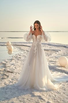 a woman standing in the snow with her arms behind her head wearing a wedding dress