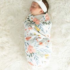 a baby wrapped in a blanket laying on top of a white rug