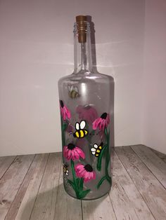 a glass bottle painted with pink flowers and bees on the bottom is sitting on a wooden floor