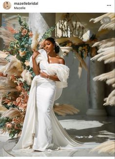 a woman in a white wedding dress standing next to a tall tree with feathers on it