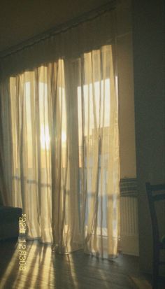 the sun shines through sheer curtains in an empty room with a couch and chair