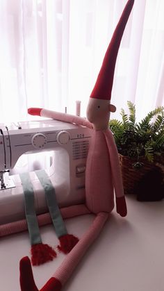 a sewing machine sitting next to a stuffed toy with a red hat on it's head