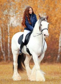 a woman riding on the back of a white horse in an open field next to trees