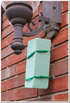 a light that is on the side of a brick building with a green box tied to it