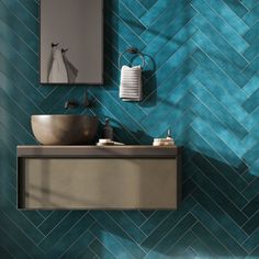 a bathroom with blue and green tiles on the wall next to a sink, mirror and towel dispenser