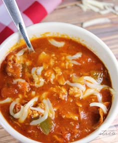 a white bowl filled with chili and meat soup sitting on top of a wooden table