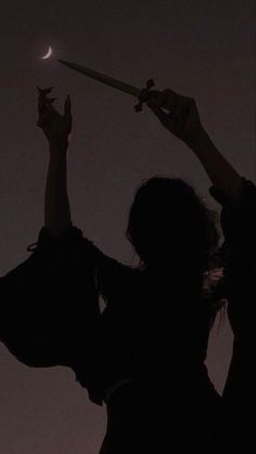 the silhouette of a woman holding a knife in her right hand and pointing at the moon