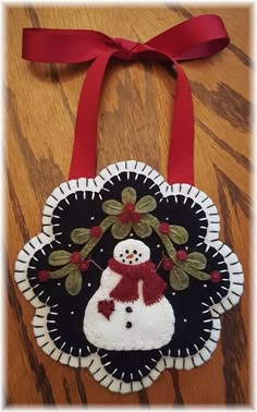 a snowman ornament hanging from a red ribbon on top of a wooden table