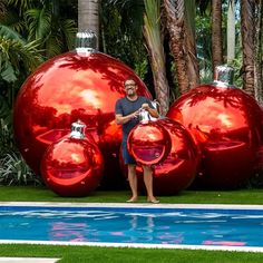 a man standing in front of three shiny red balls near a swimming pool with palm trees