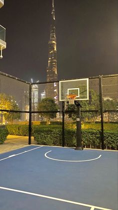 an outdoor basketball court in front of a tall building with a view of the city at night