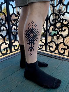 a person with a tattoo on their leg standing in front of a fence and looking at the camera