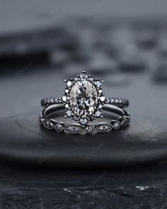 an oval shaped diamond engagement ring set on top of a black stone slab, with the center surrounded by smaller round diamonds