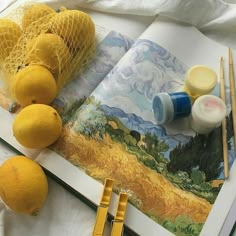 an open book with some lemons on top of it and paint brushes next to it