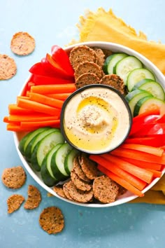 a white bowl filled with crackers and veggies on top of a blue surface