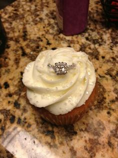 a cupcake with white frosting and a diamond ring on it sitting on a table