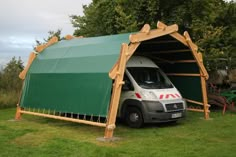 a white van parked in front of a green covered structure on the side of a field