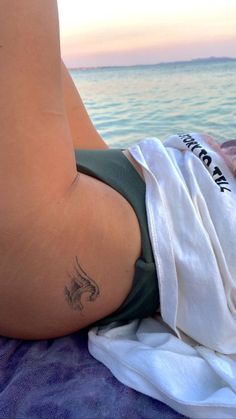 a woman laying on top of a bed next to the ocean with a tattoo on her stomach