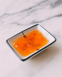 a square bowl filled with orange liquid on top of a white countertop next to a marble wall