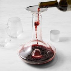 a wine glass filled with red wine being poured into the bottom of a decanter