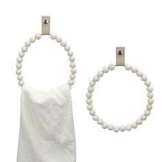 two wooden beaded rings hang from hooks on a white wall next to a towel