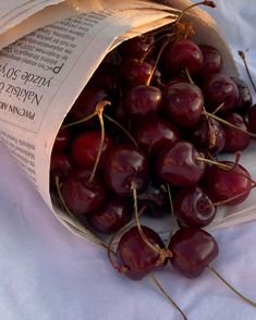 a bag full of cherries sitting on top of a white table cloth next to an open book