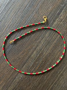 a red, green and gold beaded necklace on a wooden surface with a golden clasp