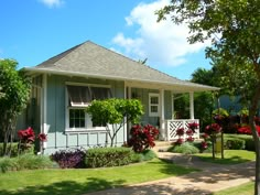 a blue house with red flowers in the front yard and landscaping around it on a sunny day