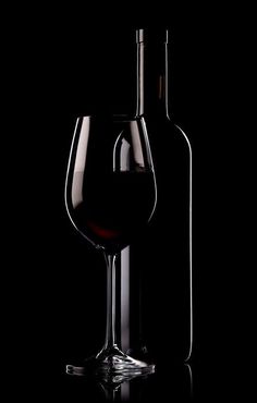 a wine glass and bottle sitting next to each other on a black surface with a dark background