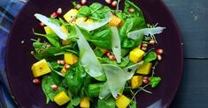 a purple plate topped with spinach and mangos on top of a blue table cloth