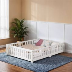 a white bed frame sitting on top of a wooden floor next to a potted plant