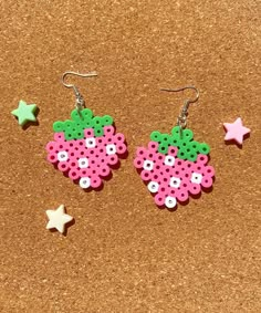 two pink and green earrings sitting on top of a cork board next to star shaped beads