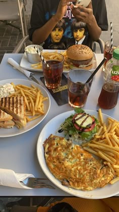 a table topped with plates of food covered in french fries and burgers next to drinks