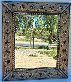 a decorative mirror hanging on the wall in front of a blue wall with trees and grass