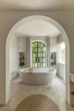 a large white bathtub sitting under an arched window next to a rug on the floor