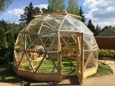 a wooden greenhouse with glass walls and plants in the garden area on a sunny day