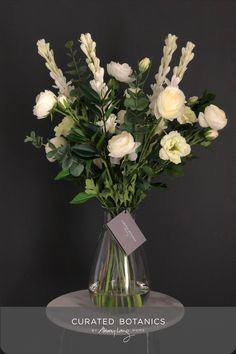 a vase with white flowers and greenery on a glass table, against a black background