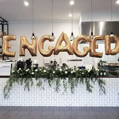 an engaged sign above a counter with flowers and greenery in front of it on the wall