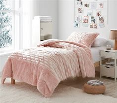 a bed with pink comforter and pillows in a white room next to a window