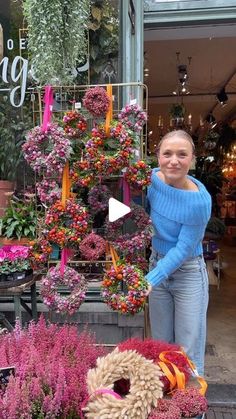 a woman standing in front of a flower shop with wreaths and flowers on display