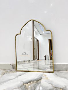 a mirror sitting on top of a marble floor next to a white wall with gold trim