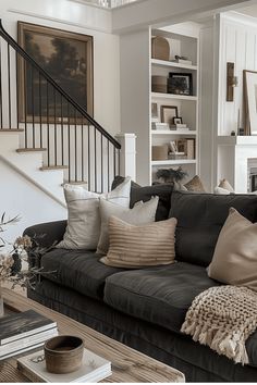 a living room filled with black couches and pillows next to a stair case full of books