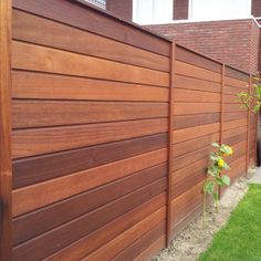 a wooden fence in front of a brick building with green grass and flowers on the side