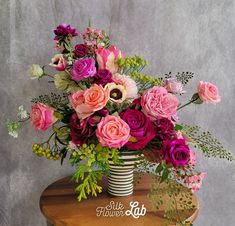 a vase filled with lots of pink and purple flowers on top of a wooden table