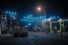 an empty city street at night with lights strung over the buildings and cars parked on the road