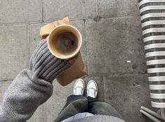 a person is holding a cup of coffee on the ground with their feet up and legs crossed