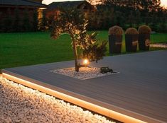 a small tree is lit up in the middle of a patio area with gravel and rocks