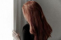 a woman with long red hair standing in front of a window looking out the window