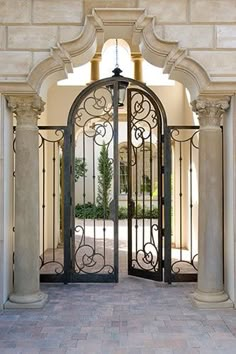 an ornate iron gate is open to the front yard and courtyard area, with stone pillars on either side