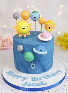 a blue birthday cake with smiley faces on it and candles in the shape of planets