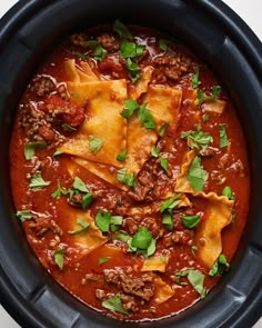 a black crock pot filled with meat and tortilla shells covered in sauce